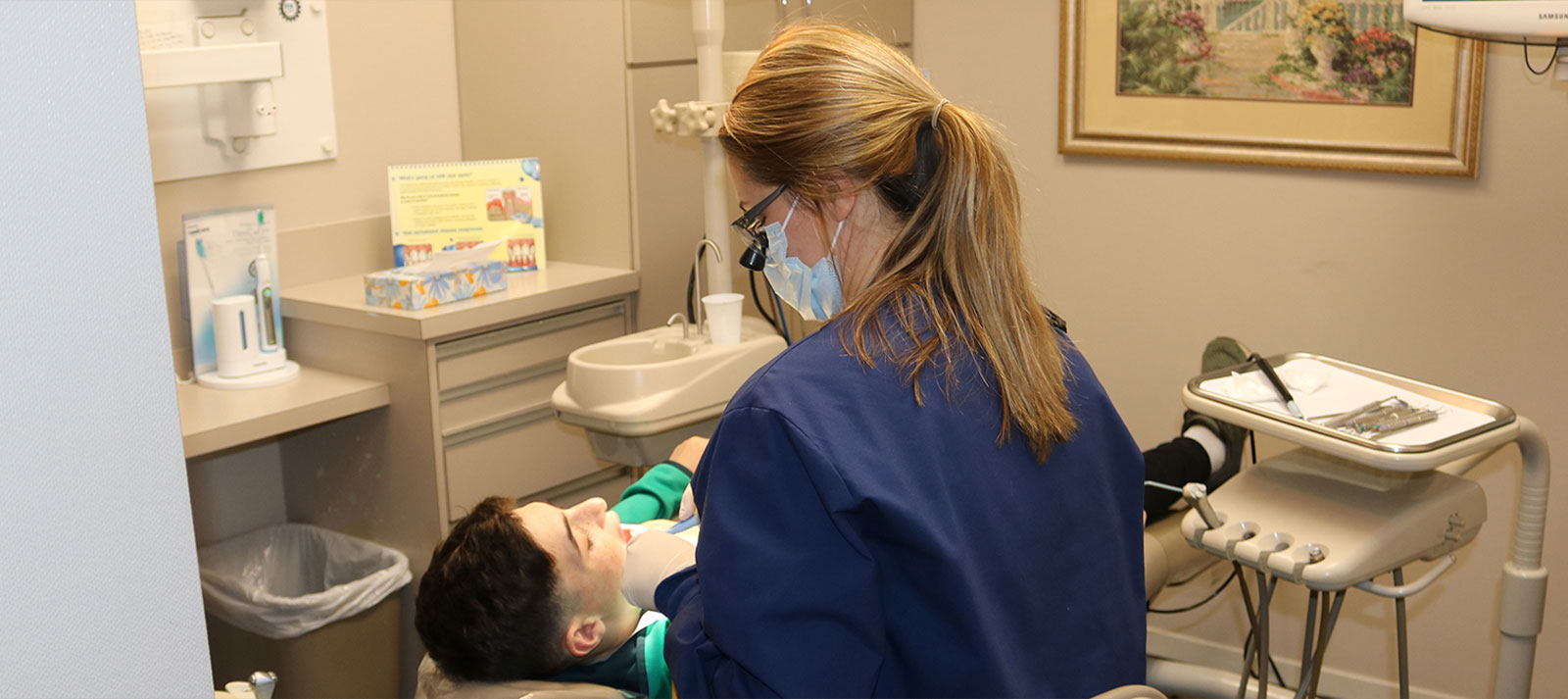 Dental hygiene professional performing a dental cleaning on a patient in an office setting.