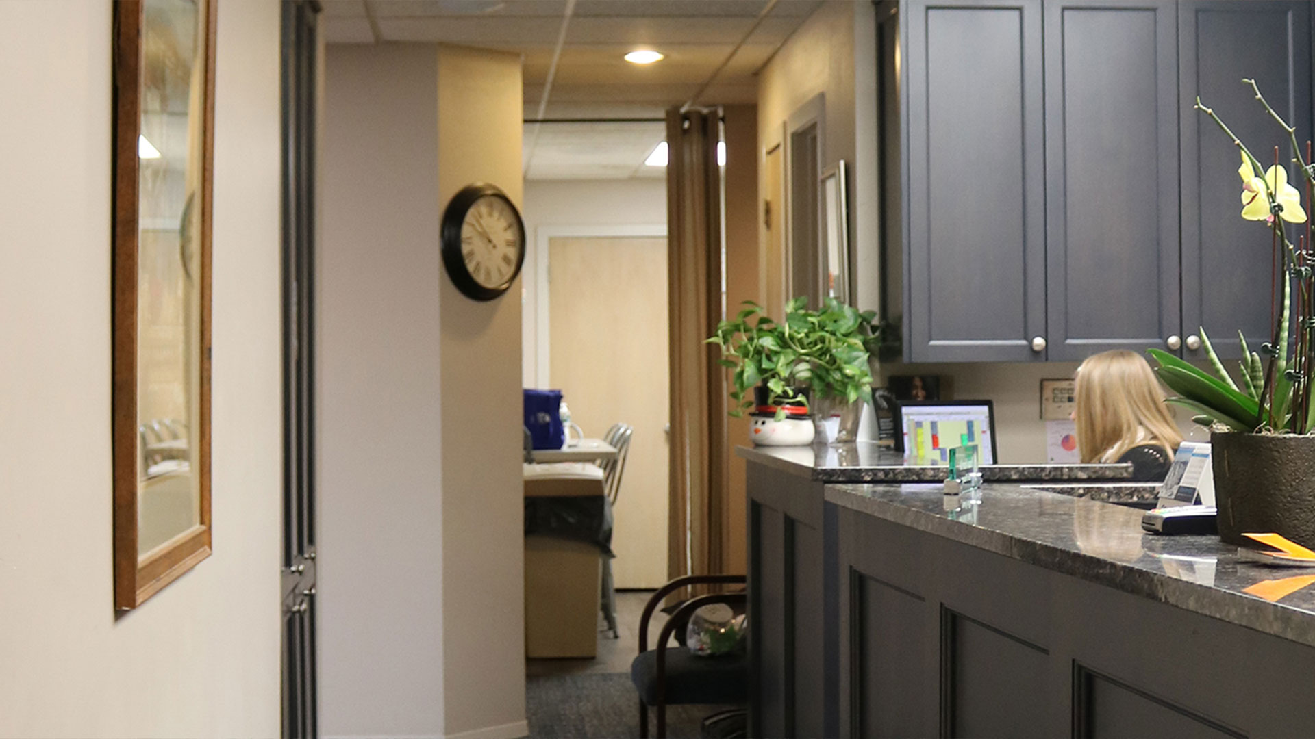 An image of a well-lit, modern office interior with a reception area, featuring a desk, chair, potted plant, and framed artwork on the wall.