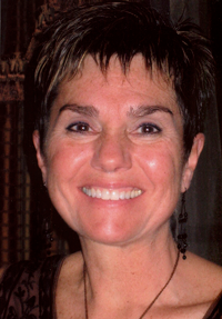 The image shows a woman with short hair, wearing a dark top and a necklace, smiling at the camera.