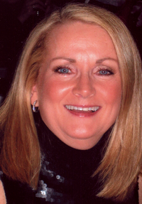 A woman with blonde hair and a smile, wearing a black top, poses for the camera.