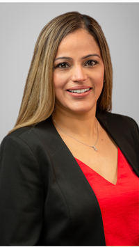 A woman in a black suit stands confidently against a white background, smiling and looking directly at the camera.