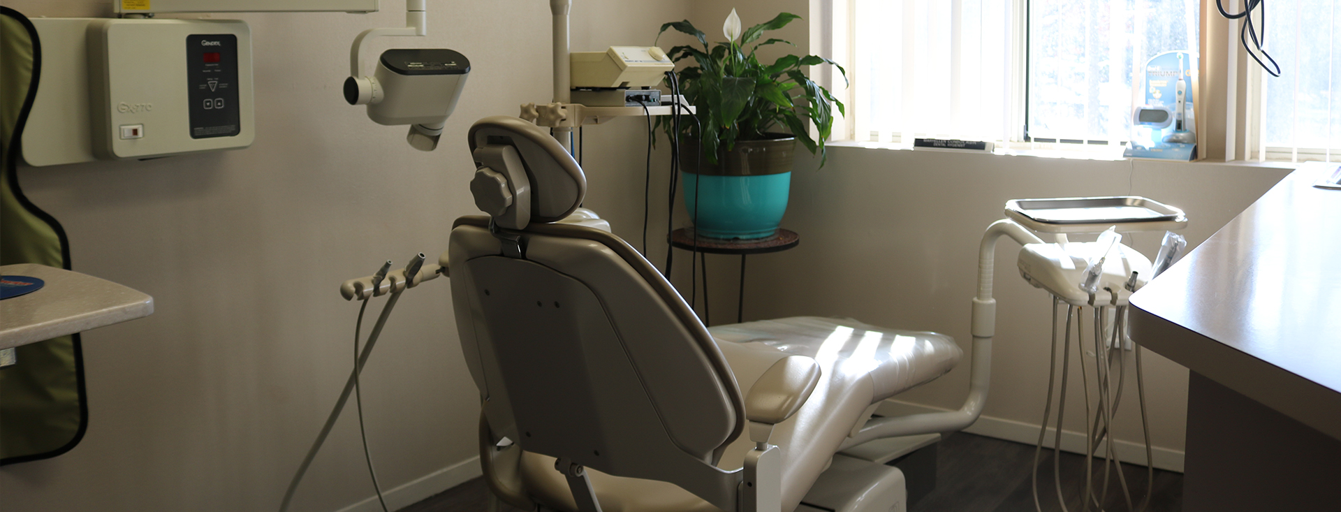 The image shows a dental office interior with a dental chair, equipment, and a desk.