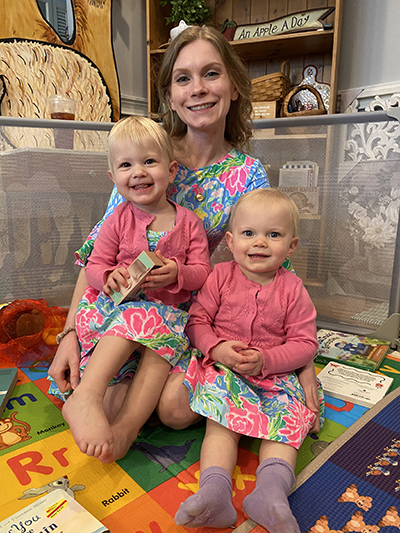 A woman and two children are sitting on the floor, smiling at the camera.