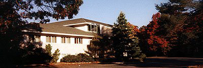 The image displays a two-story residential house with a white exterior, a prominent front door, and a clear view of the surrounding area.