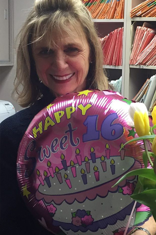 A woman holding a balloon with a message of congratulations on her 16th birthday.