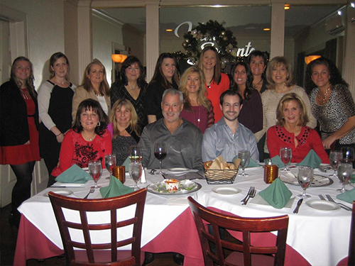 This is a photograph of a group of people posing for a picture at a restaurant, with a festive atmosphere indicated by the decorations and attire.