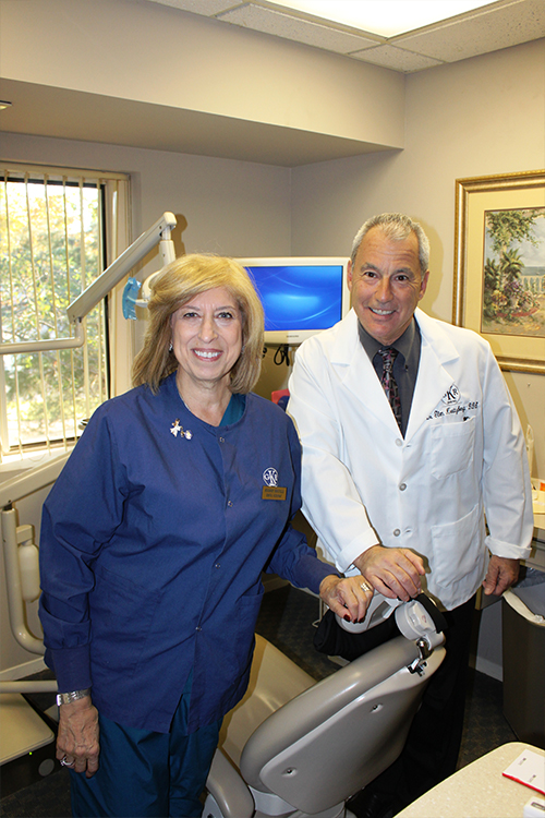 A man and woman, both in professional attire, standing together in a dental office setting.