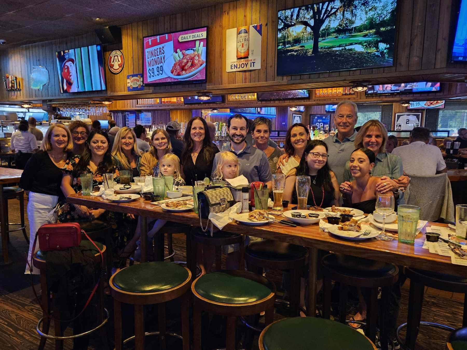 A group of people gathered around a dining table in a restaurant, posing for a photo with drinks and food on the table.