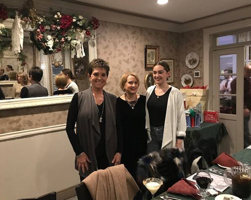 Three individuals posing for a photo in a restaurant setting, with one person seated and two standing behind a dining table.