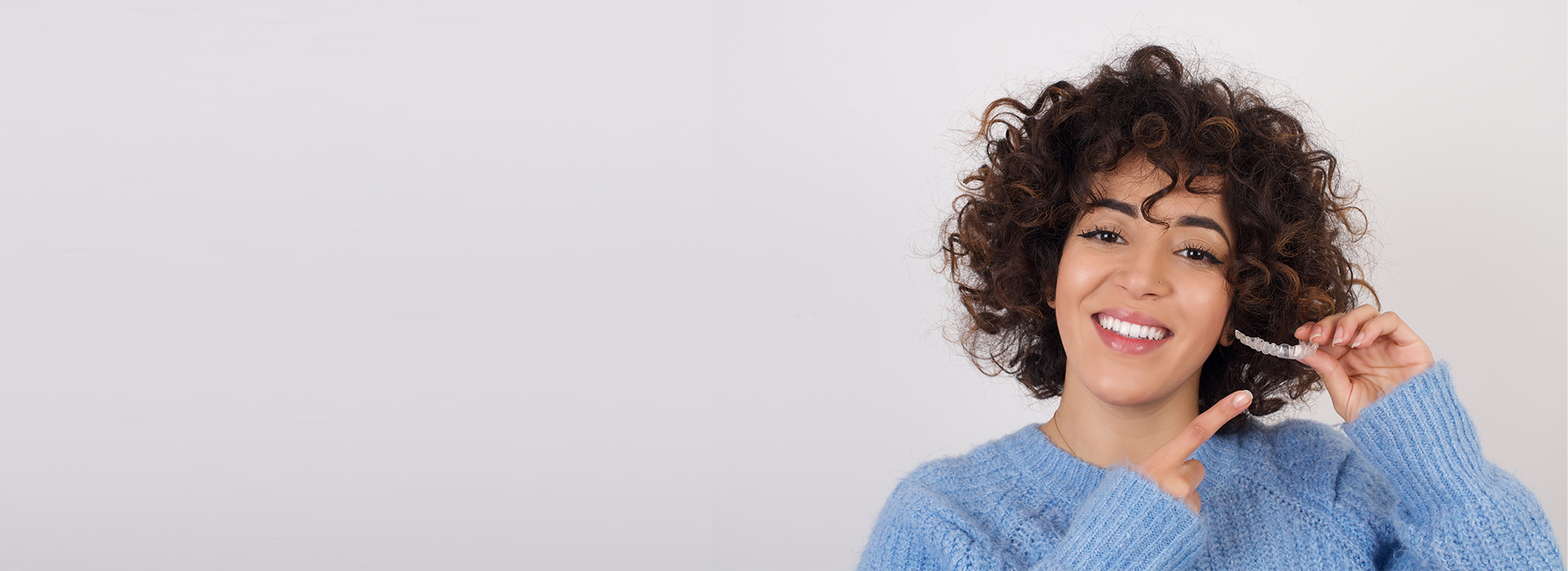 A person with curly hair, smiling, and holding a phone to their ear.