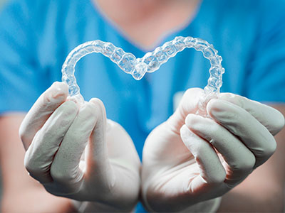 The image shows a pair of clear plastic braces held by a person s hands, with a heart-shaped symbol placed on the braces.