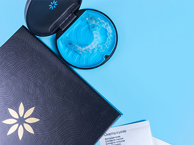 A blue toothbrush with a matching case, placed on top of an open black box with a white logo, set against a blue background.