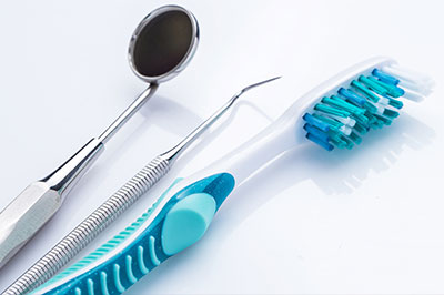 The image shows a collection of dental tools, including a toothbrush with blue bristles and a pair of metal scissors, arranged on a white background.