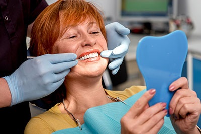 A woman is sitting in a dental chair, receiving dental care with a smile, while holding up a blue mouthguard.