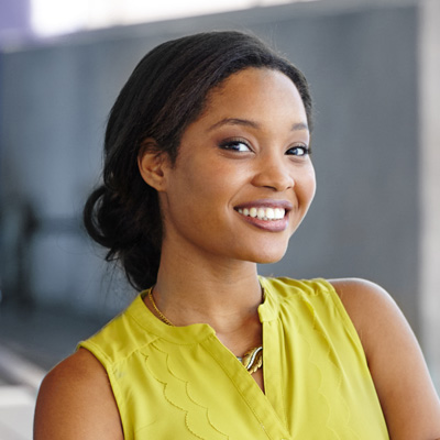 A young woman with a radiant smile, wearing a yellow top and posing against a backdrop.