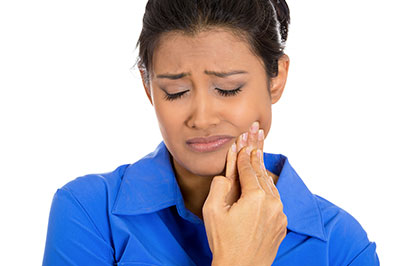 A woman in a blue shirt, wearing a mask and showing concern or worry on her face, is looking down at her hand which is holding something small.