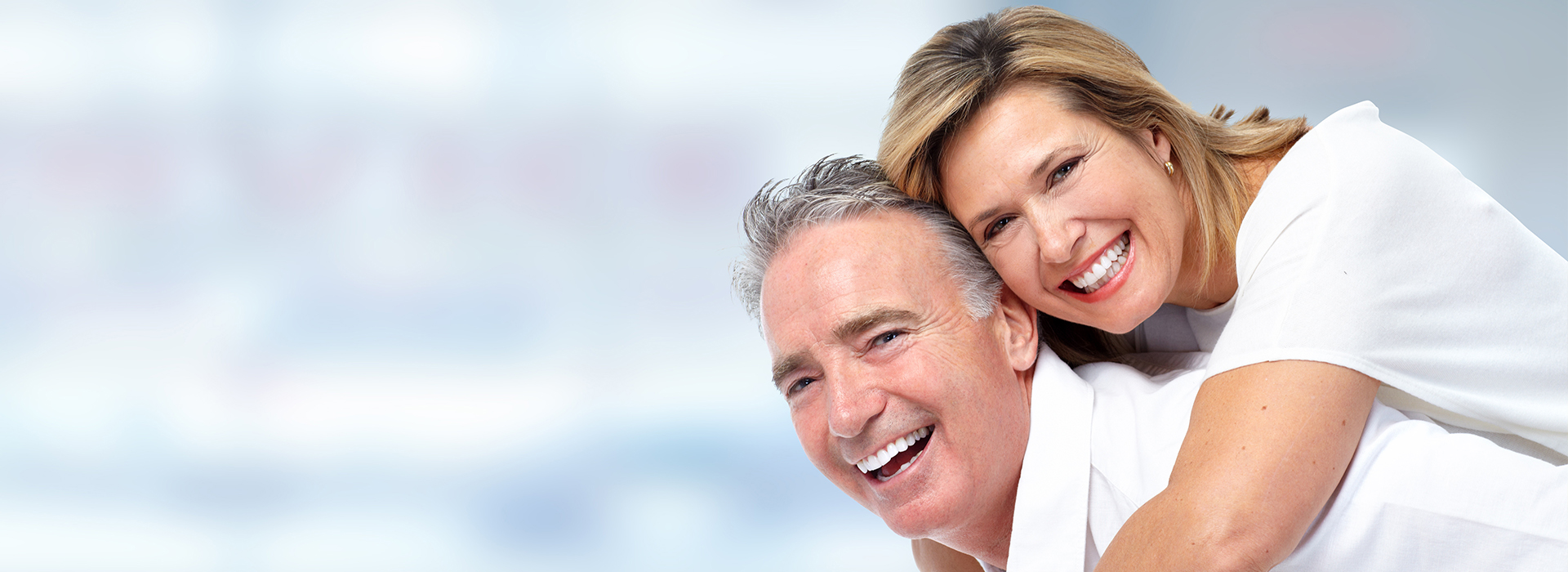 The image is a photograph of an older couple, with the man in white and the woman in light blue, smiling at each other, embracing, and looking into the camera.