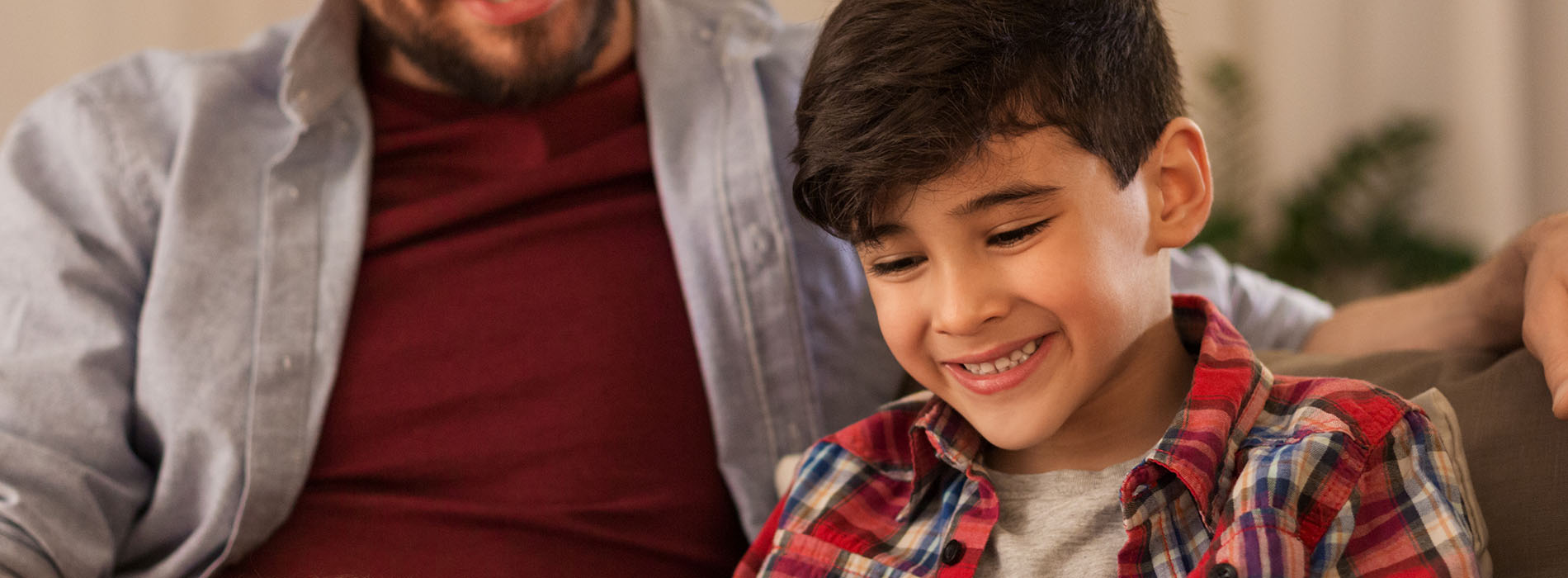 A man and a child are seated, looking at a device with smiles on their faces.