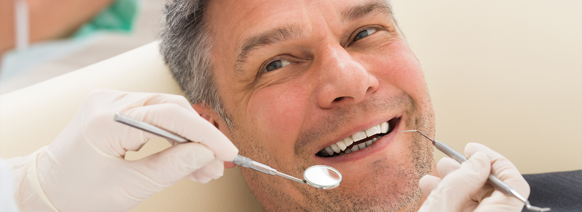 A man in a dental chair receiving dental treatment, with a smiling expression and white gloves visible.