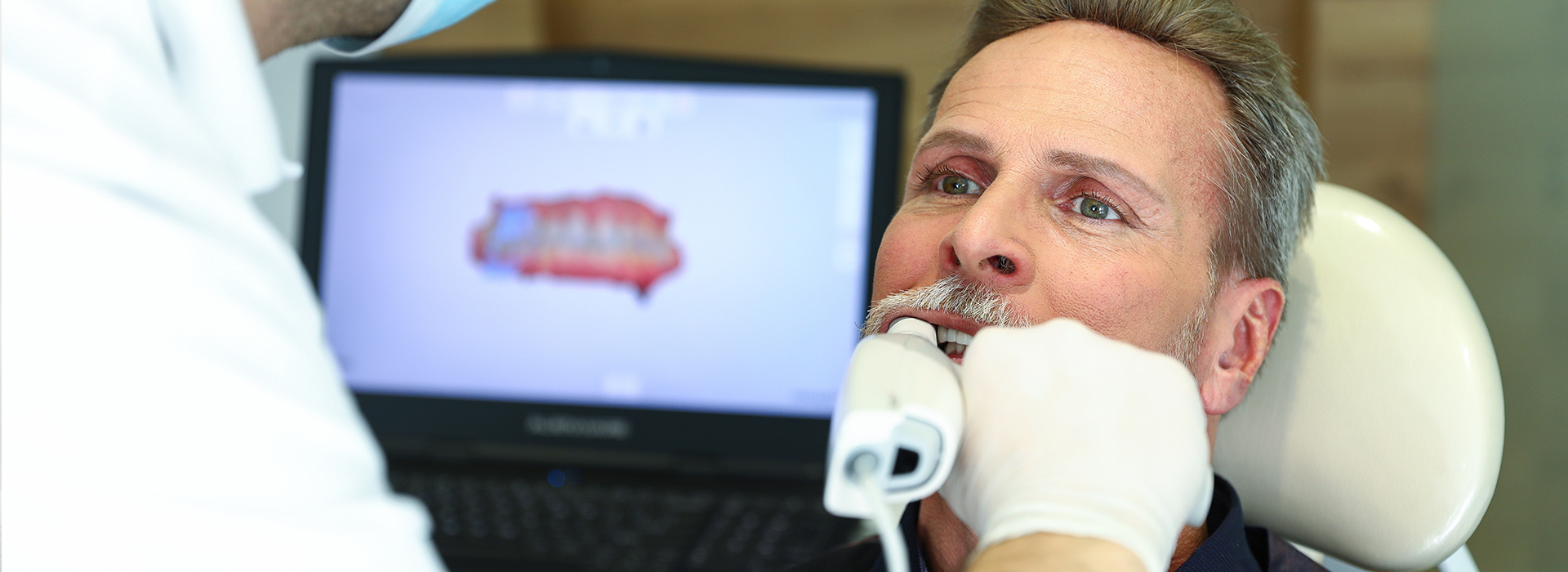 An image of a man receiving dental care, with a dental professional using a computer screen to guide the procedure.