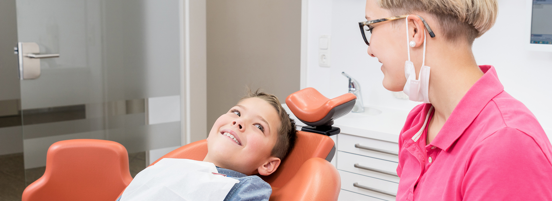 A dental hygienist assisting a child in a chair during an oral examination.