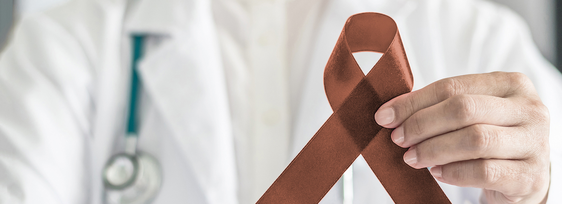 The image shows a person holding a red ribbon with a white cross symbolizing the medical profession, in front of a grey background.