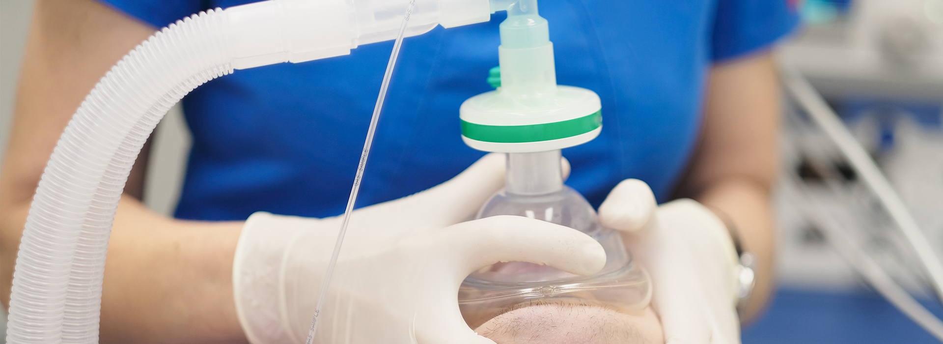 The image shows a person wearing gloves and handling a clear plastic bottle with a green cap, which appears to be connected to a transparent tube system.