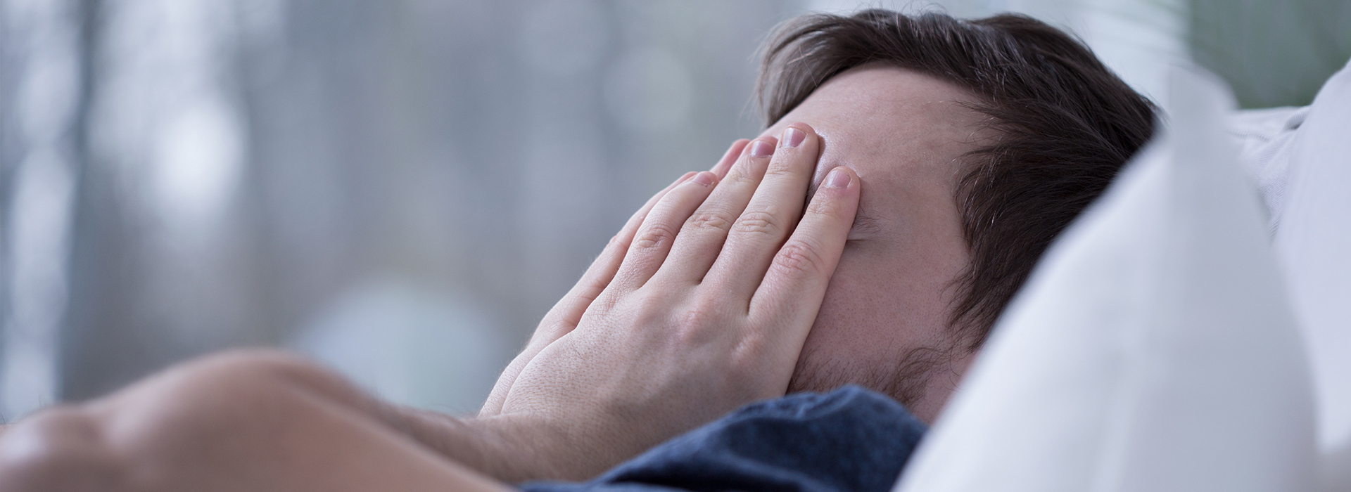 A person lying in bed with their face covered by a hand.