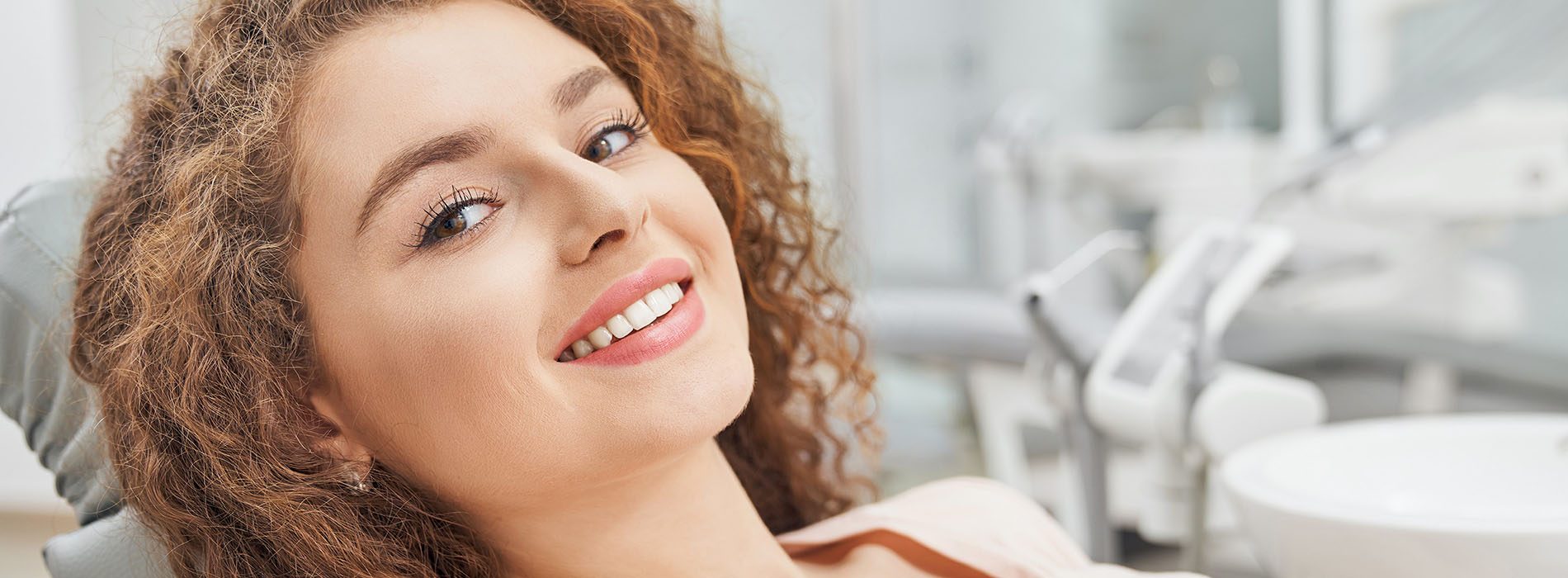 A woman is seated in a dental chair, smiling towards the camera.