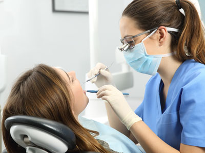 The image shows a dental professional performing an oral procedure on a patient, with the dentist using specialized equipment and wearing protective gear.