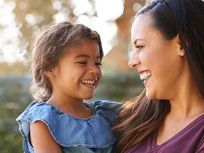 A smiling woman holding a young child, both looking at the camera with joyful expressions.