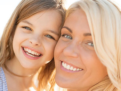 The image shows a woman and a young girl smiling at the camera, with the woman s face partially obscured by the child s head.
