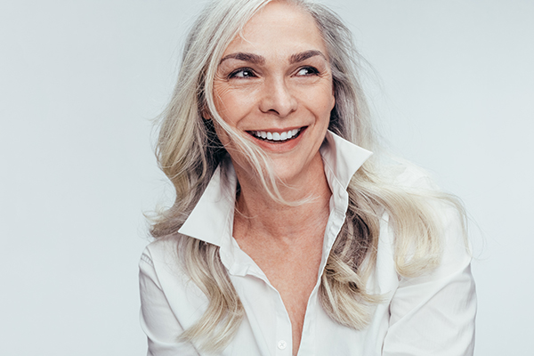 The image shows a woman with short hair, wearing a white top and smiling at the camera.