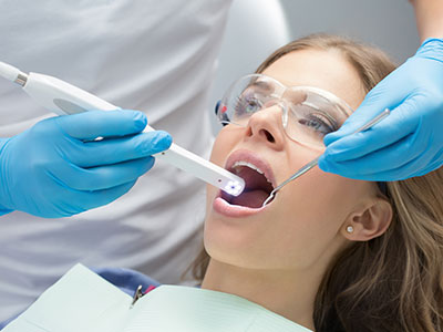 A dental professional is performing a teeth cleaning procedure on a patient, using an electric toothbrush and wearing protective gloves.