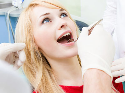 A woman receiving dental care, with a dental professional performing a procedure while the patient is wearing protective eyewear and a surgical mask.