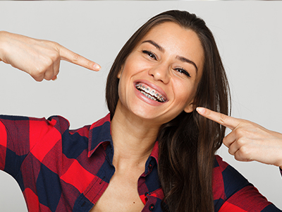 A woman with a wide smile pointing to her teeth, showing off her dental implants.